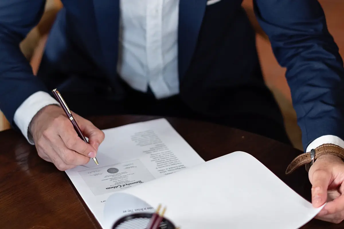 Pessoa de terno assinando documento com caneta sobre a mesa