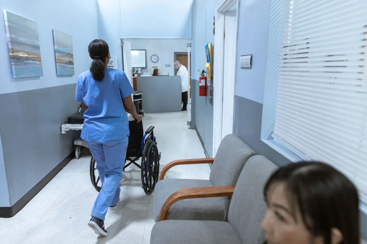 Enfermeira empurrando uma cadeira de rodas pelo corredor de uma clínica