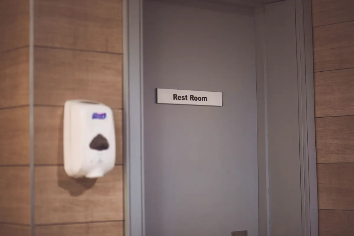 Dispensador de sabonete na parede ao lado da porta de um sanitário com placa