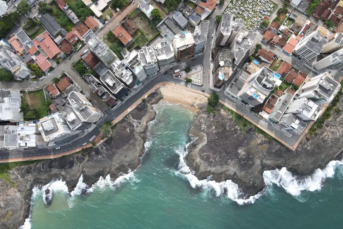 Vista aérea de uma enseada de Guarapari cercada por prédios e casas, com ondas nas pedras