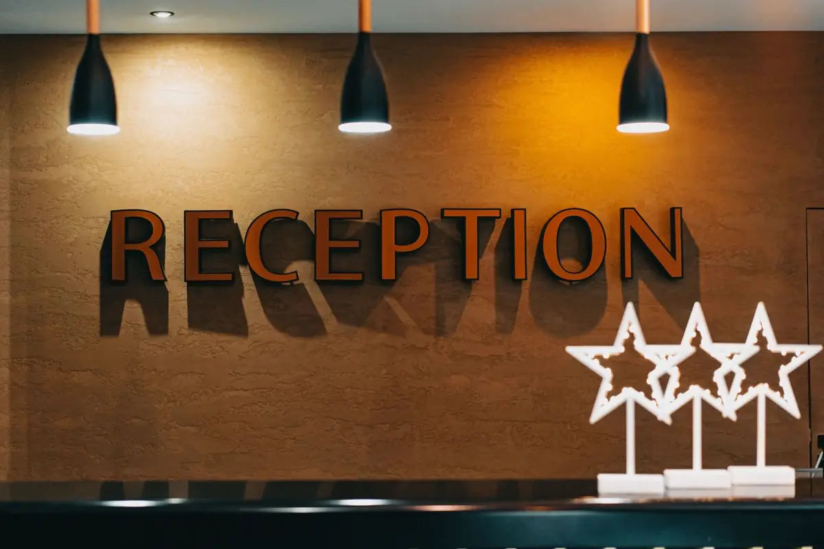 Balcão de recepção de hotel com letreiro na parede de madeira e luminárias pendentes