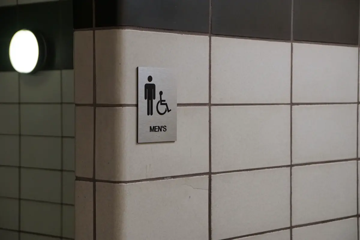 Placa de sanitário masculino com símbolo de acessibilidade na parede revestida