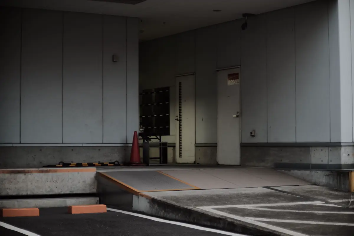 Entrada de prédio com acesso em rampa suave até a porta, ao lado da área de garagem