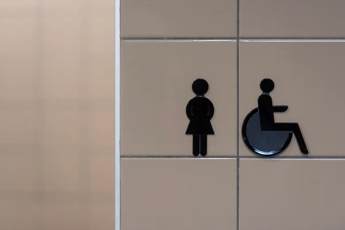 Placa de sanitário com pictograma feminino e símbolo internacional de acesso em parede revestida