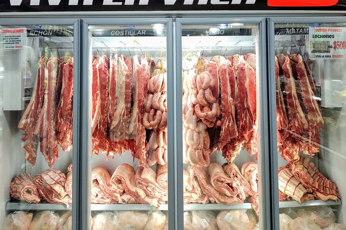 Expositor refrigerado de portas de vidro com cortes de carne e linguiças pendurados em ganchos e peças embaladas nas prateleiras de baixo