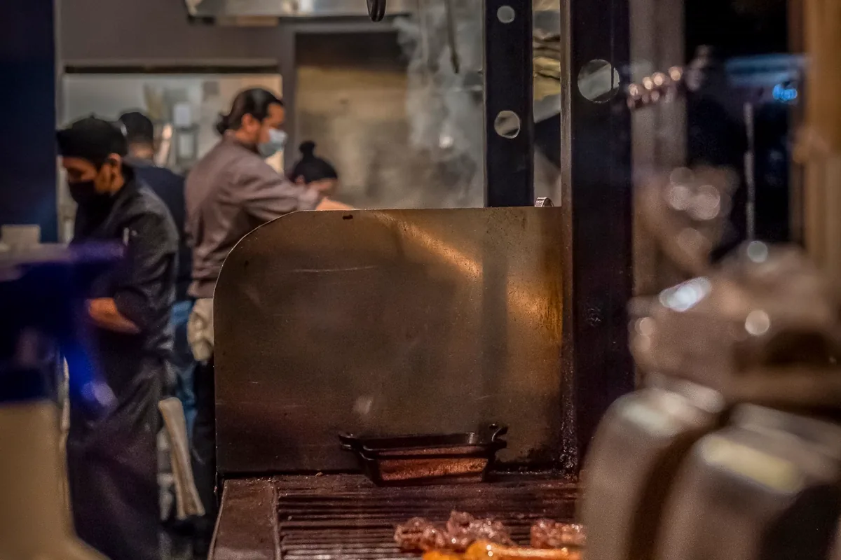 Cozinha industrial em operação, com coifa sobre a linha de fogões e equipe trabalhando