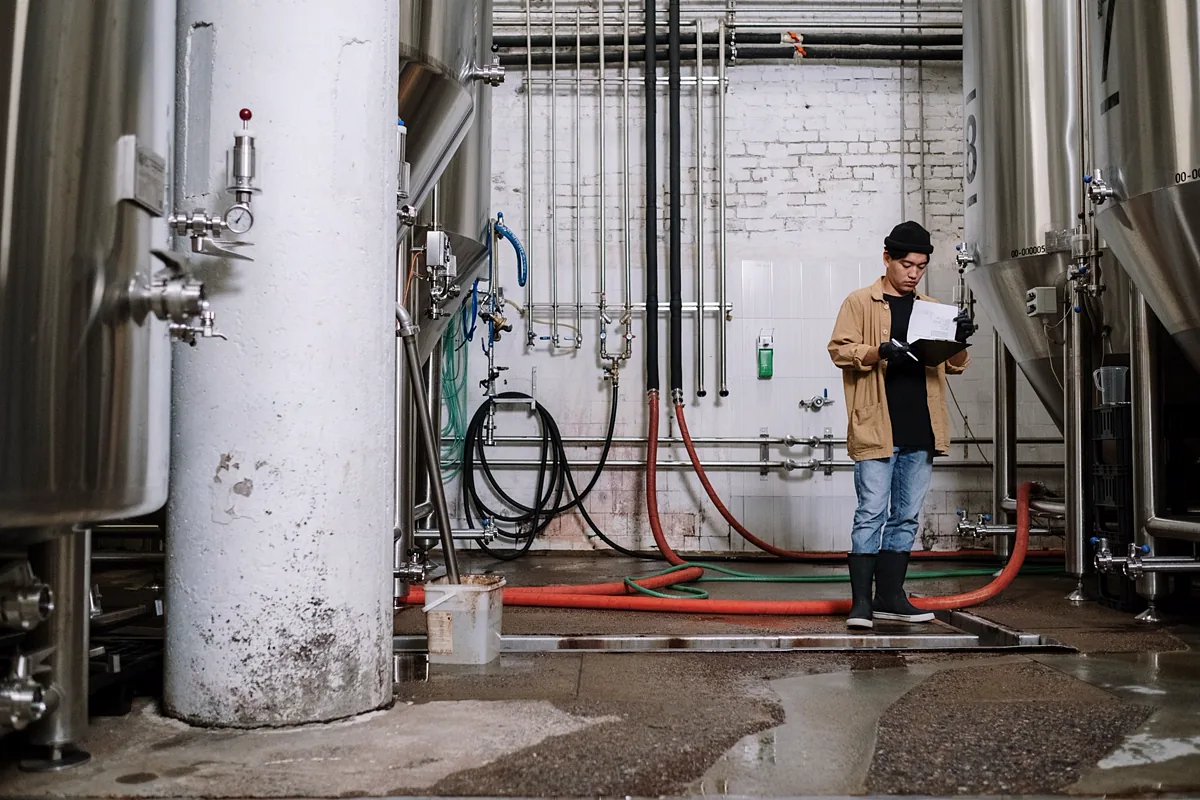 Técnico de inspeção anotando dados em prancheta ao lado de tanques e tubulações em planta industrial