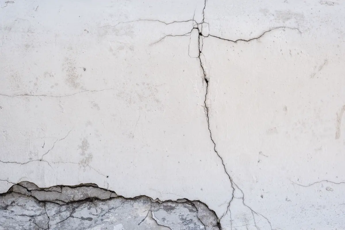 Fissuras ramificadas numa parede de concreto pintada de branco