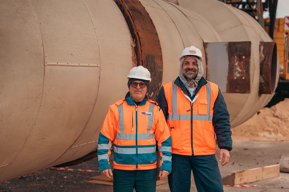 Dois técnicos de inspeção uniformizados em frente a um vaso de pressão de grande diâmetro em área industrial