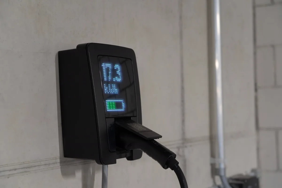Detalhe de estação de recarga de veículo elétrico instalada em parede, com o cabo conectado