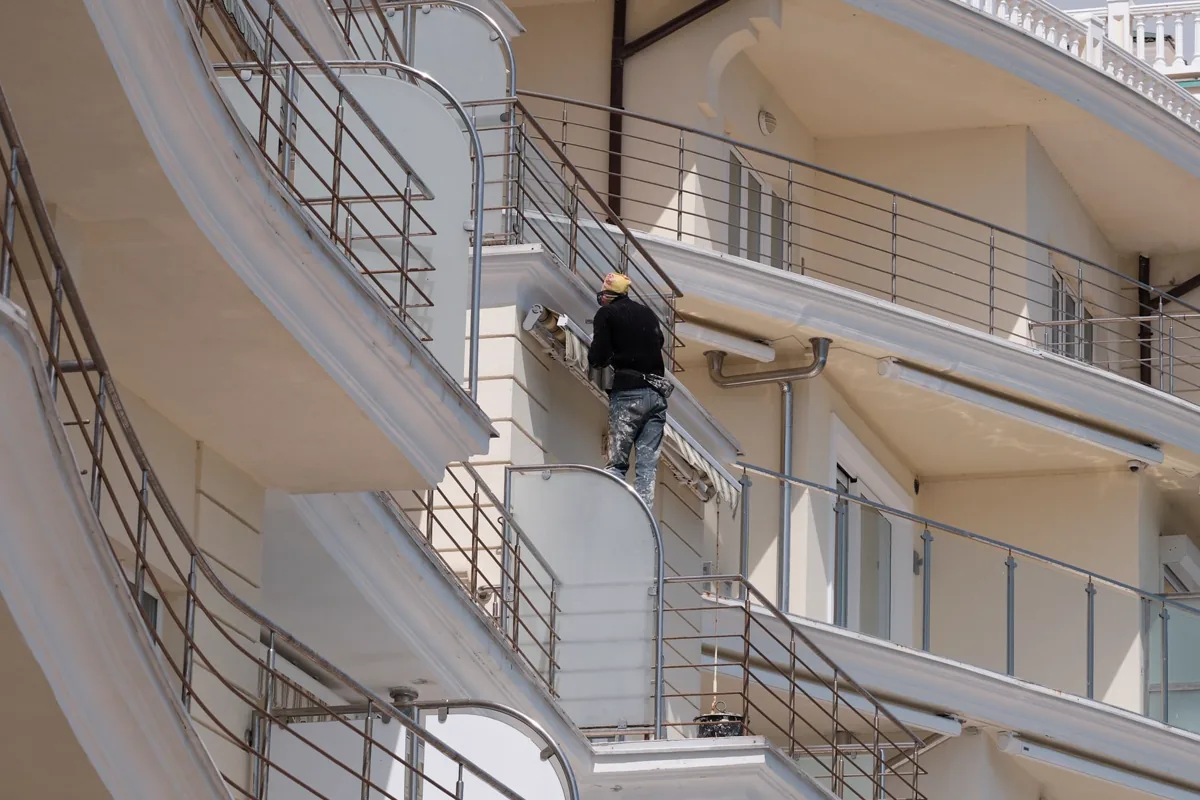 Profissional executando serviço de manutenção na varanda e na fachada de um edifício residencial