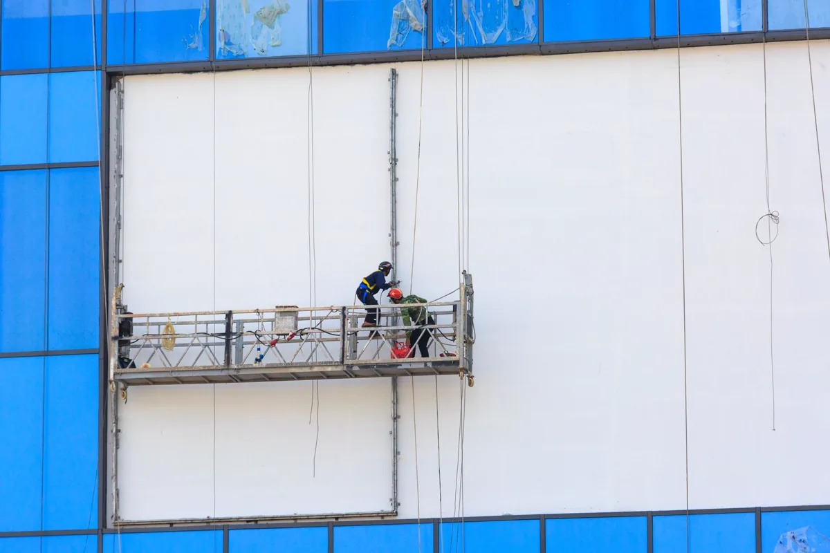 Dois profissionais em andaime executando reparo e pintura da fachada de um edifício