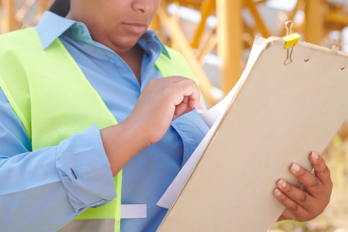 Engenheira com capacete e colete de segurança conferindo documentos em prancheta durante vistoria técnica