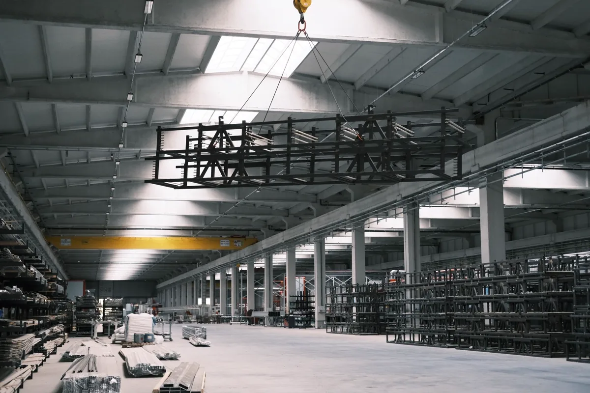 Interior de galpão industrial com ponte rolante amarela içando carga sobre a área de produção