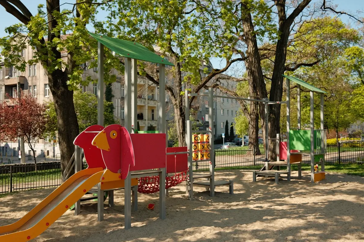 Playground de área comum com escorregador e área de queda em areia, cercado por árvores