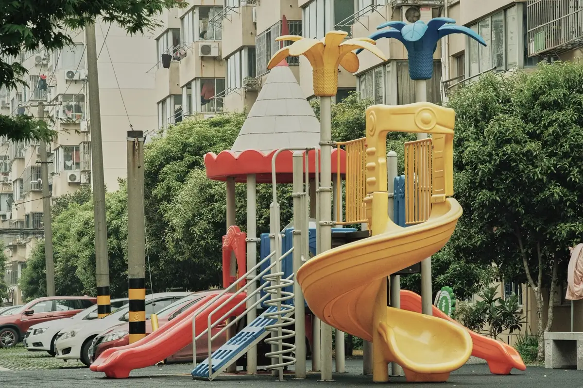 Conjunto de escorregadores e plataformas de playground urbano, com prédios residenciais ao fundo